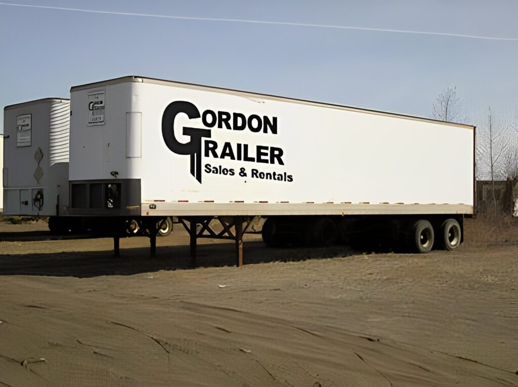 A white trailer truck parked in the middle of a lot.