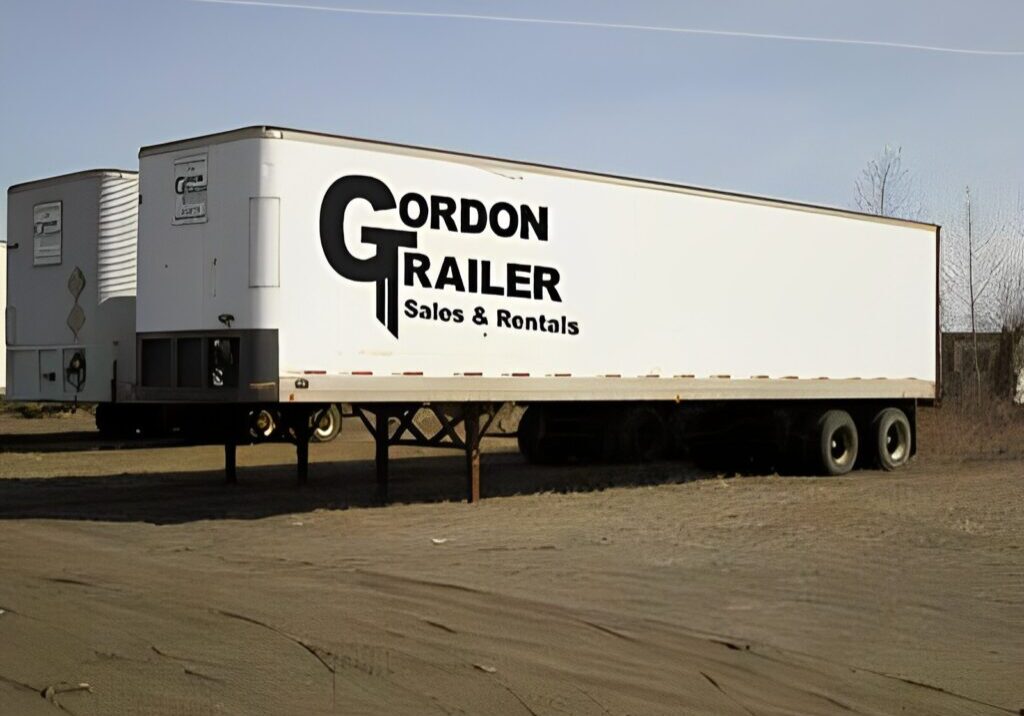 A white trailer truck parked in the middle of a lot.